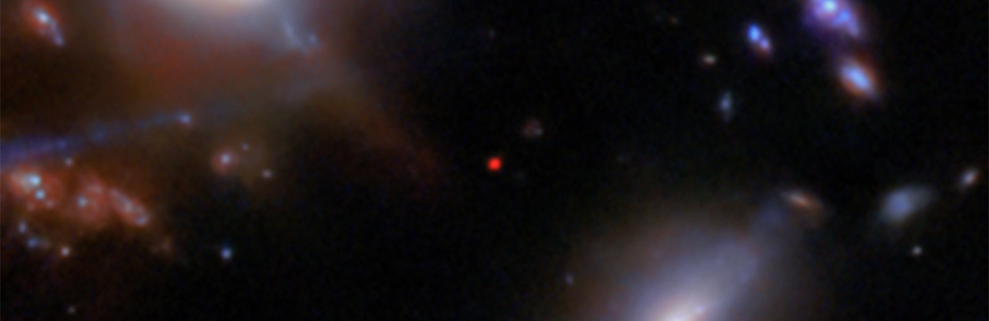 Several blurry galaxies of various sizes and shapes on a black background in this image from the JWST. In the center, a small red dot marks the most distant galaxy in this field, JADES-GS-z13-1.