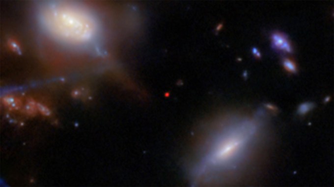 Several blurry galaxies of various sizes and shapes on a black background in this image from the JWST. In the center, a small red dot marks the most distant galaxy in this field, JADES-GS-z13-1.