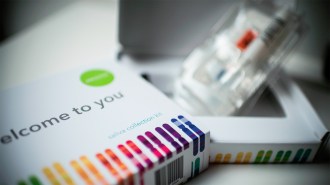 A saliva collection kit biox sits in the foreground, while its contents can be seen in the background slightly blurred. Millions of 23andMe customers have used these DNA testing kits.