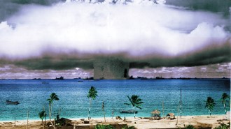 The smoke plume from a nuclear test in Bikini Atoll along a beach front.