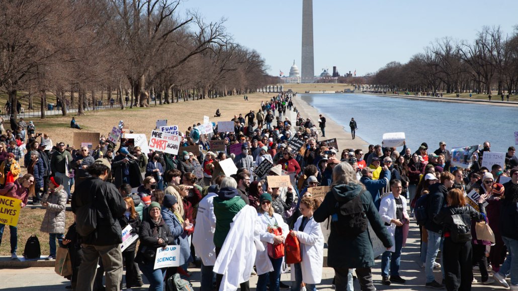 A crowd gathers along the reflecting pool carrying signs in support of science.