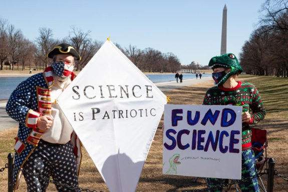 People hold signs reading "Science is patriotic" and "Fund science."