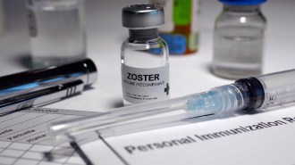 A vial containing a vaccine is located on a table next to a syringe.