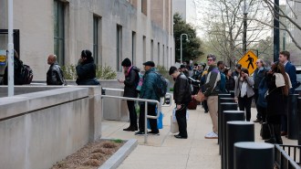 Lines of people stand waiting to get into a big gray federal building.