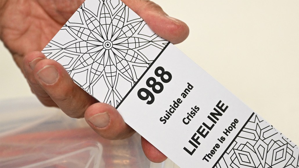 A photo of a hand holding a card that reads "988 Suicide and Crisis Lifeline There is Hope"