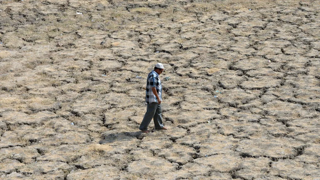 A man in a blue shirt and pants walks across a dry cracked lake bed.