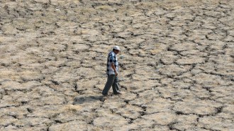 A man in a blue shirt and pants walks across a dry cracked lake bed.