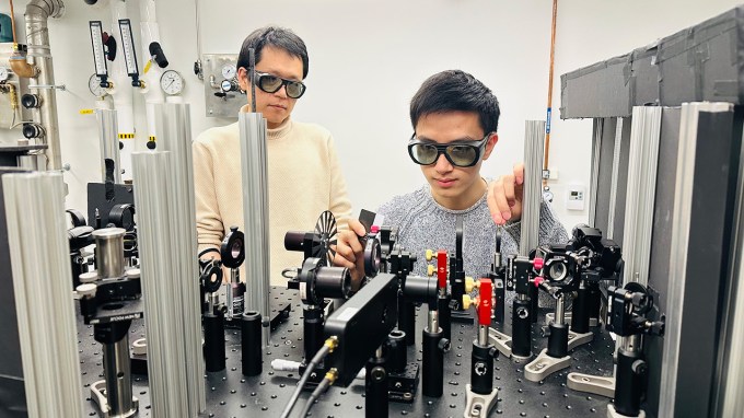 A photo of researchers Suyang Xu (left), Jianxiang Qiu (right) in safety goggles standing in front of lab equipment.