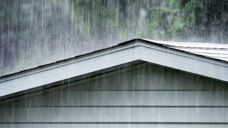 A photo shows raindrops falling on a shingle roof.