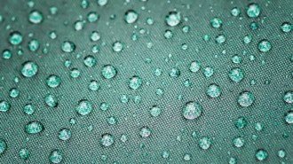 A close up of a dark green umbrella with water beading on it.