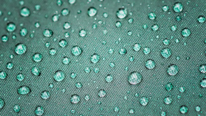 A close up of a dark green umbrella with water beading on it.