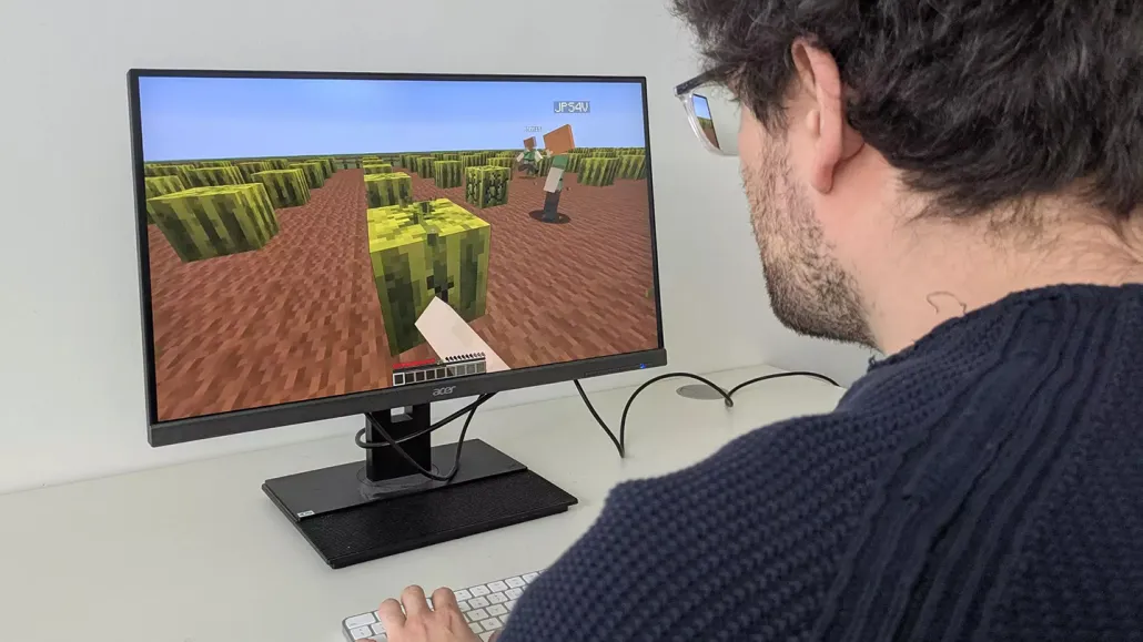 A man with brown hair looks at a computer screen, which shows a digital scene filled with blocks.