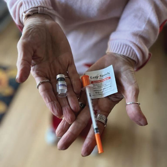 A woman holds her prescription of the compounded weight-loss drug tirzepatide to show what comes in the kit, which includes a syringe about the length of her hand with an orange safety tip and a tiny bottle of the liquid medicine about half the size of her thumb.