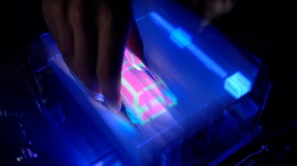 a hand reaches down into an illuminated screen displaying a virtual 3-D graphic of a car