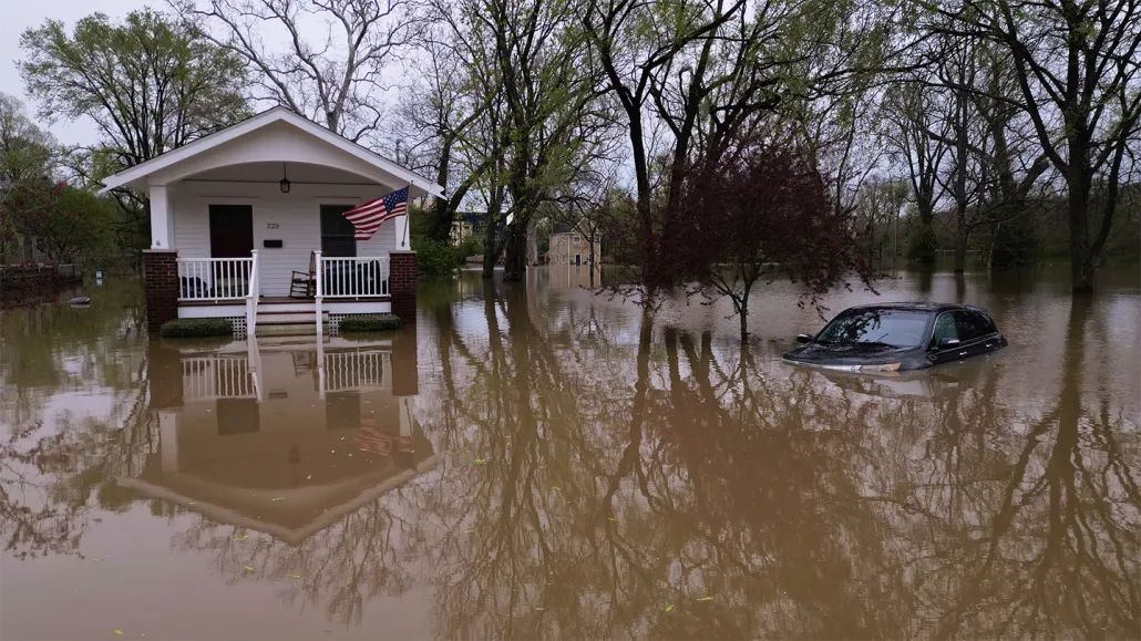 Muddy-looking water surrounds a car and house, creeping up toward the car windows and the steps of the front porch.