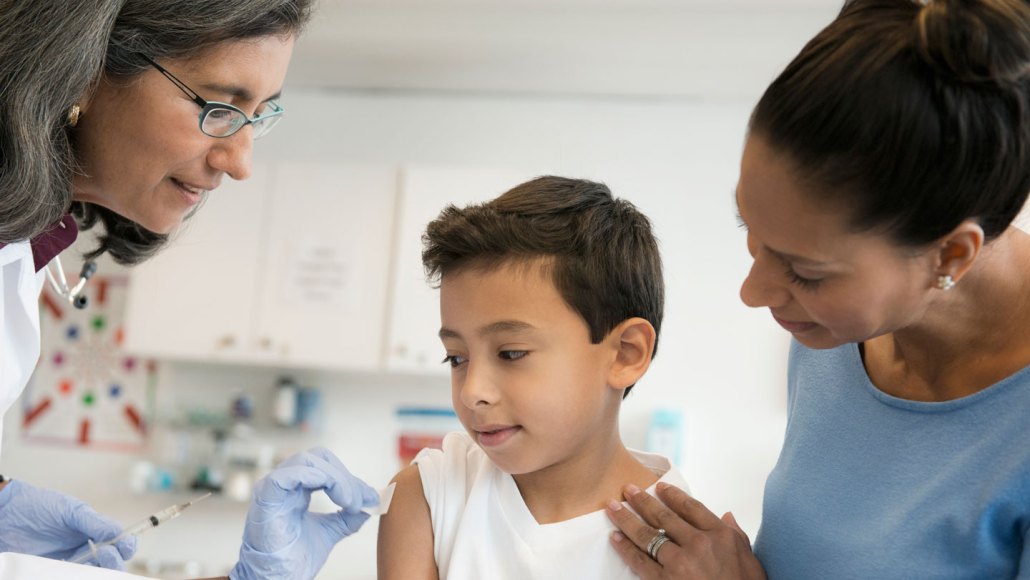 A doctor wipes an alcohol pad on a child's shoulder to prep them for a vaccine.