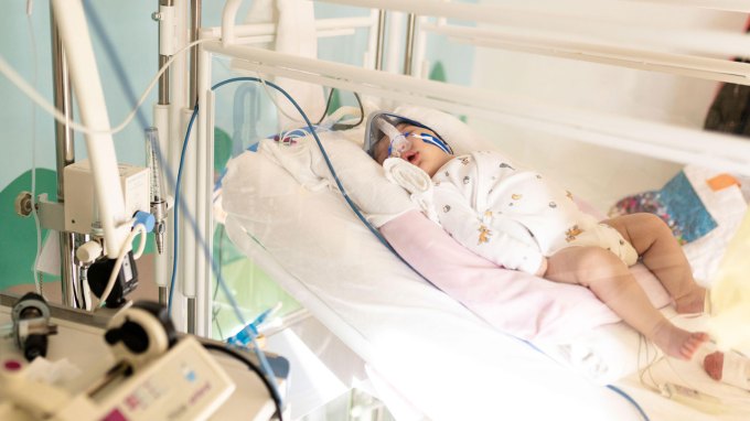 A baby lying in a hospital bed, eyes close, receiving treatment for a lung infection