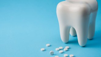 A large white ceramic tooth surrounded by white fluoride tablets against a light blue background.