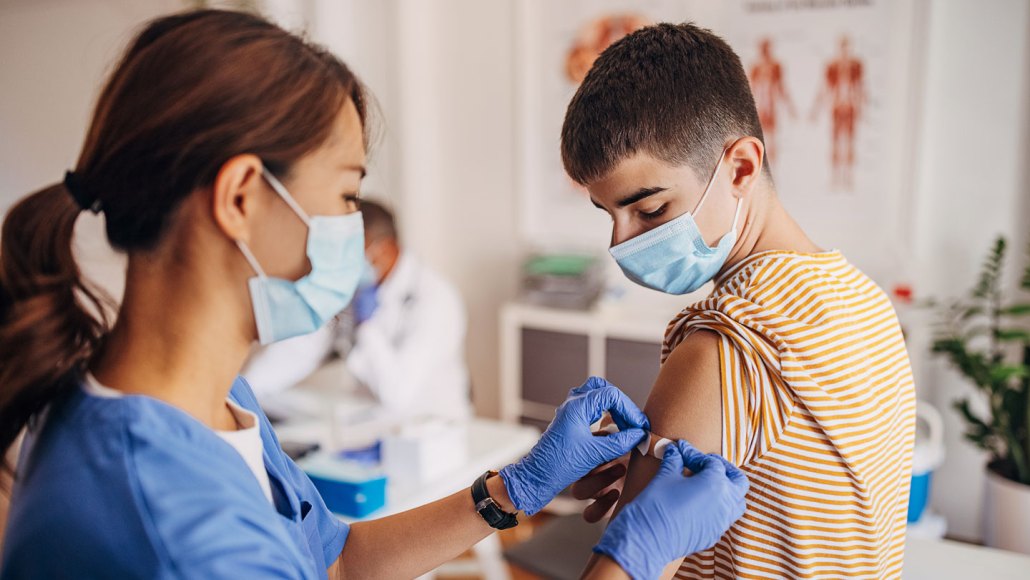 Nurse putting a bandage on a young person's arm after receiving a vaccine.