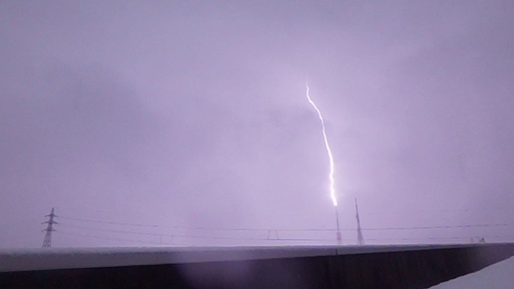 A bolt of lightning zaps a TV tower, lighting up a purple clouded stormy sky.