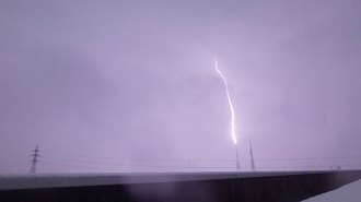 A bolt of lightning zaps a TV tower, lighting up a purple clouded stormy sky.