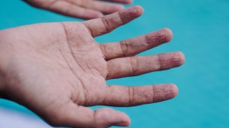 A hand with wrinkly fingertips held above a swimming pool.