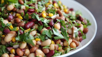 A bean salad including chickpeas, kidney beans, corn and parsley in a white plate. This could be part of a healthy diet.