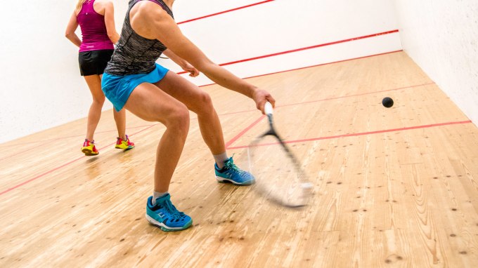 A person prepares to hit a squash ball with a racket.