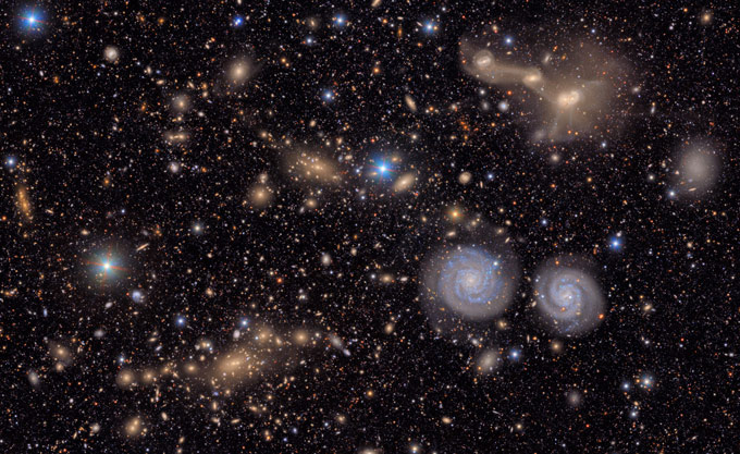 Stars and galaxies of different shapes and colors are scattered across the black backdrop of space.