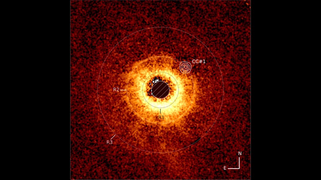 This image shows a star, center, whose light is blocked so that the surrounding dust rings are visible. Three are labeled and a spot on the edge of one is marked with concentric circles to denote the location of a purported exoplanet spotted by the Webb telescope.