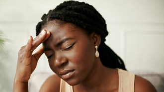 A woman with her eyes closed holds her forehead in pain.