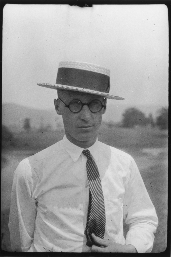 A portrait of John Scopes, seen wearing a hat, round glasses and a tie.