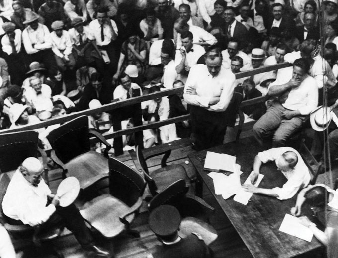 An aerial shot of a person writing on a piece of paper on a desk among a crowd of people.