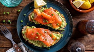 A blue plate holds two pieces of toast topped with avocado and salmon, which contain essential nutrients important for health.