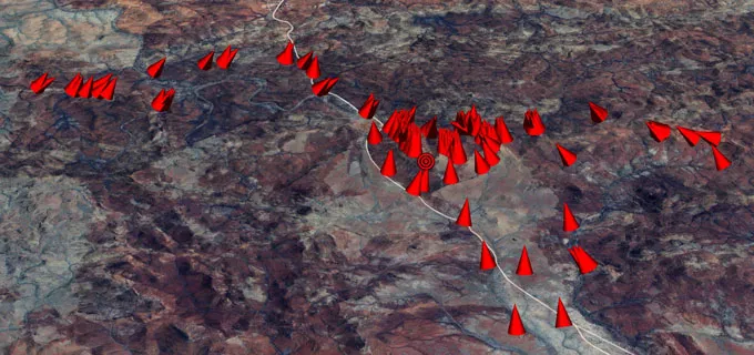 Satellite view of rocky terrain with overlaid red 3D cones pointing upward, densely clustered in the center and scattered outward. A small bullseye symbol marks the impact center.