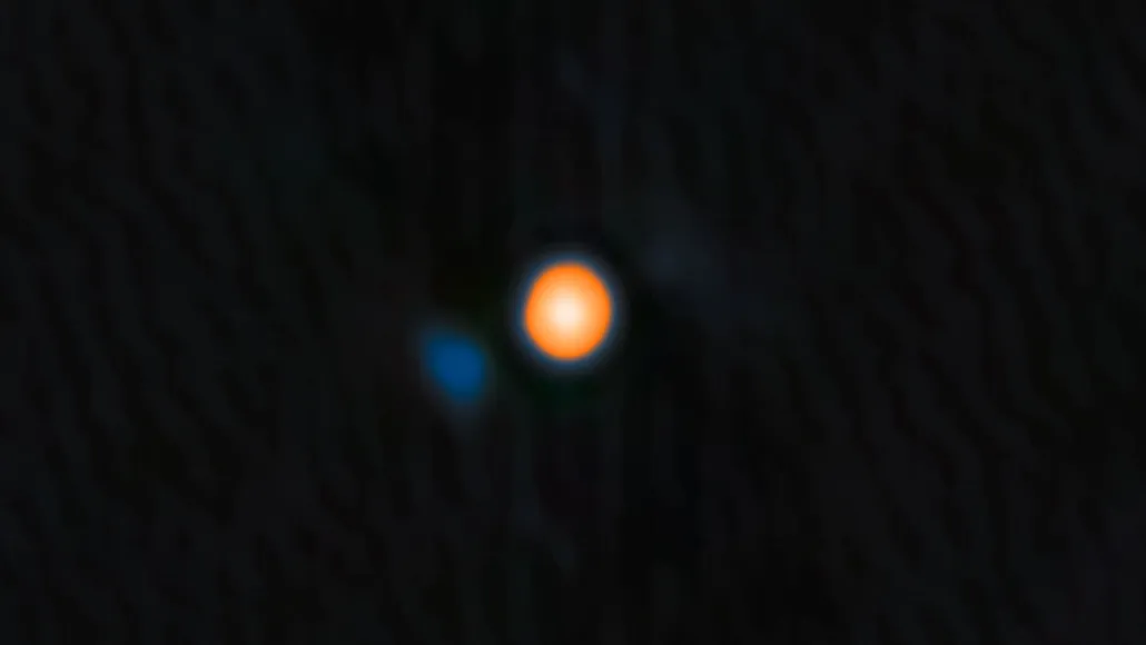 Blurry astronomical image showing the star Betelgeuse as a bright, orange circular blob against a dark background with a smaller, faint blue spot to the lower left.