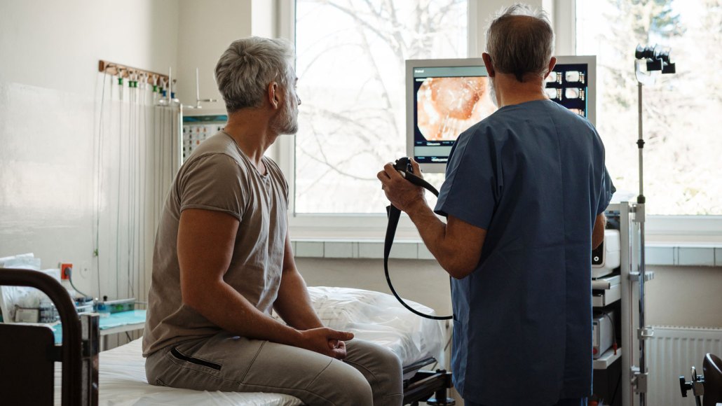 A doctor and patient in an exam room look at a screen with an image of the patient's colon