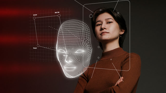 A woman stands with her arms crossed, with a 3-D diagram of her face in front of her.