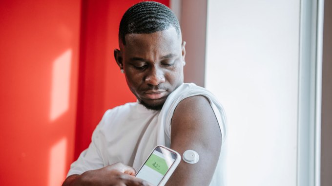 A man holds his phone near a medical device attached to his arm.