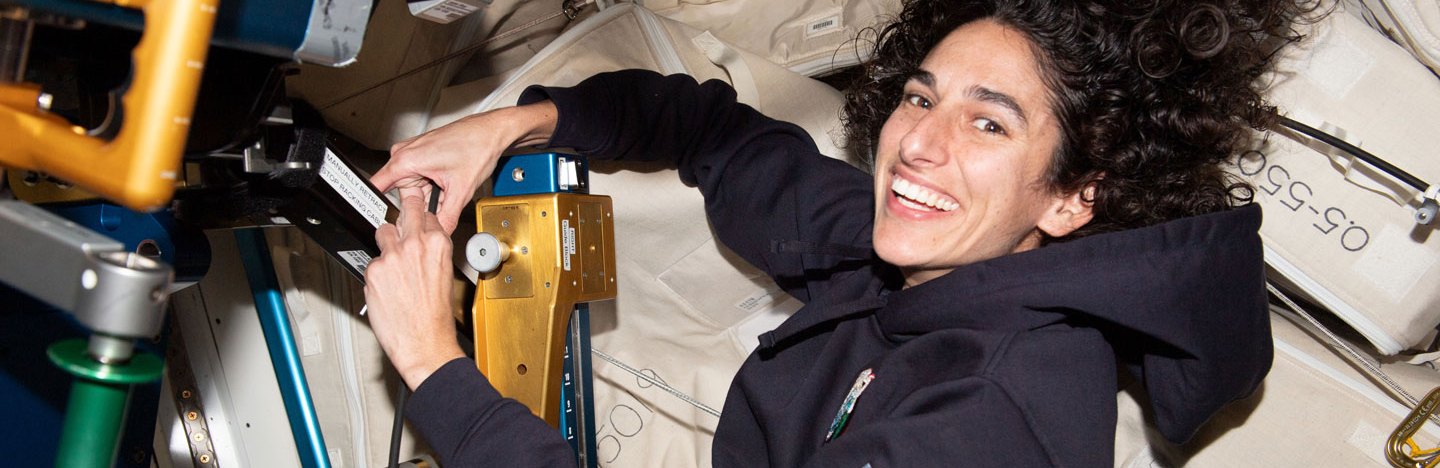 A smiling astronaut handles equipment with hair floating above her head