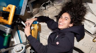 A smiling astronaut handles equipment with hair floating above her head