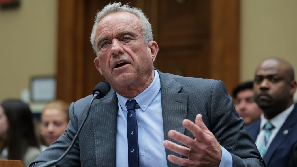 Robert F. Kennedy Jr sits in front of a microphone wearing a suit and tie.