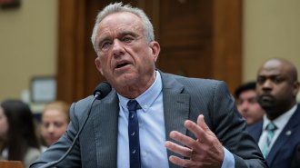 Robert F. Kennedy Jr sits in front of a microphone wearing a suit and tie.
