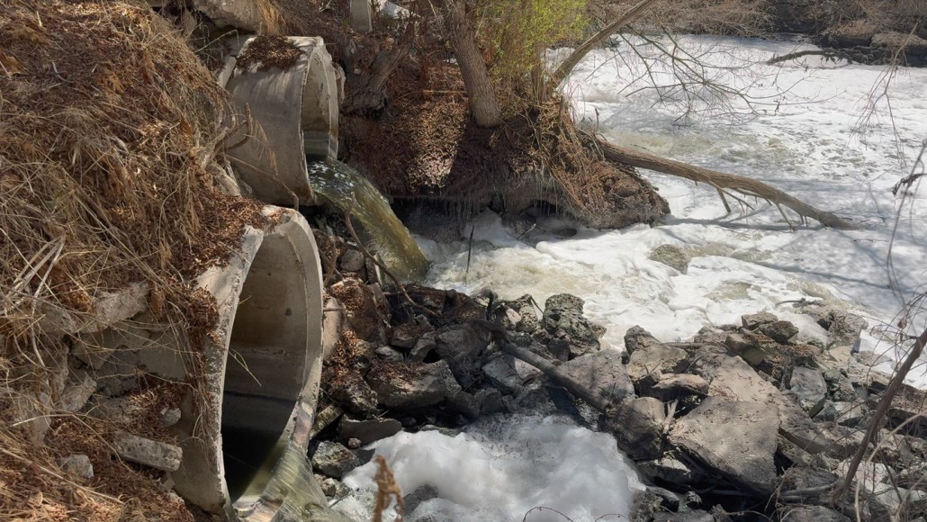 River water is shown rapidly flowing through concrete culverts, creating foam in the Tijuana River. The water appears brownish black because it is contaminated with untreated sewage.
