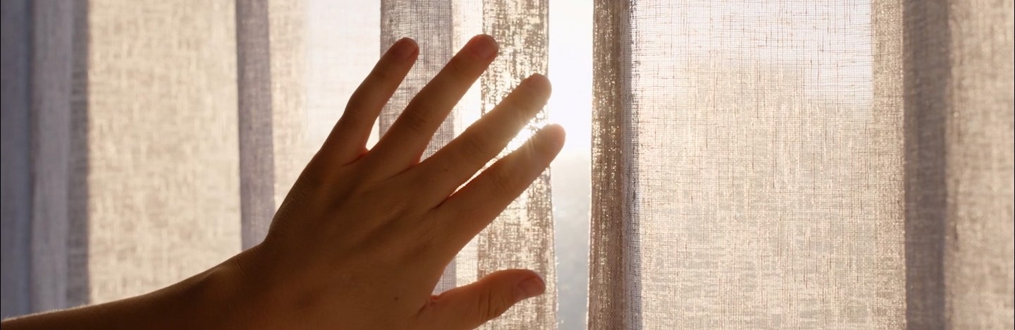 A woman's hand opens a curtain.