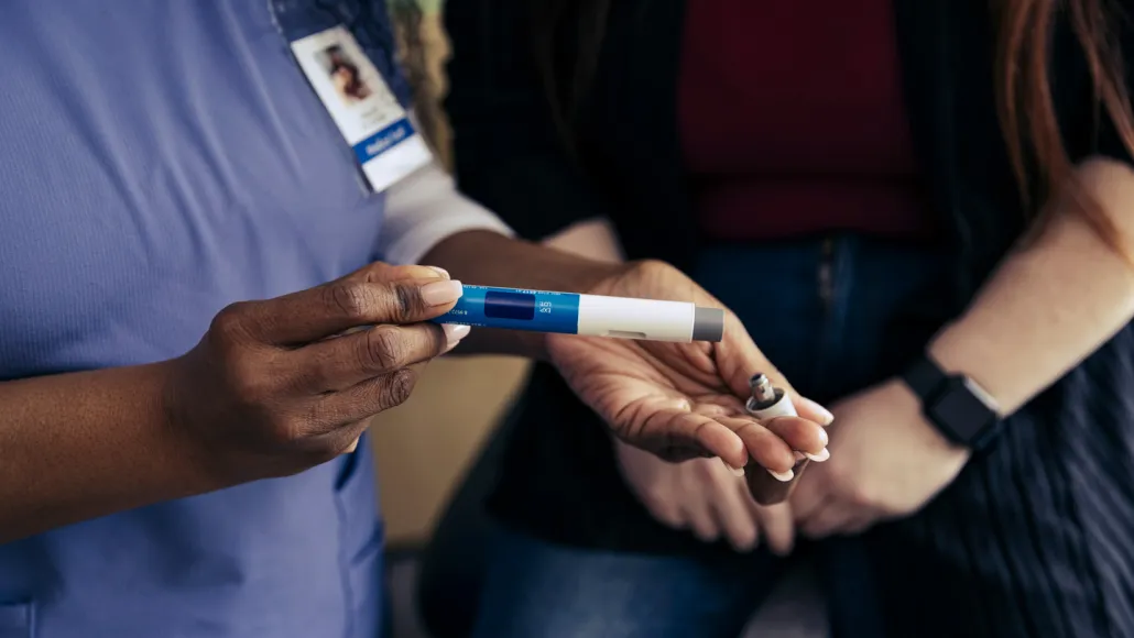 A health care worker holds a GLP-1 injector pen in front of a patient.