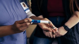 A health care worker holds a GLP-1 injector pen in front of a patient.