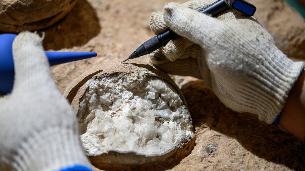 A photograph of a scientist examining a fossilized dinosaur egg filled with crystals of calcite.
