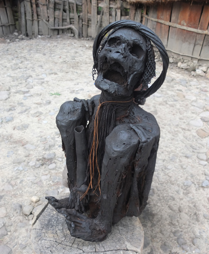 The image shows a modern-day mummified person with their jaws open and their body folded so the knees touch the shoulders.