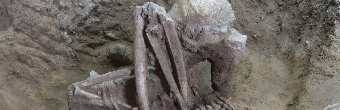 A folded up skeleton with what looks like the knees near the skull sits on dirt. Researchers say it's an example of the oldest mummies every found.